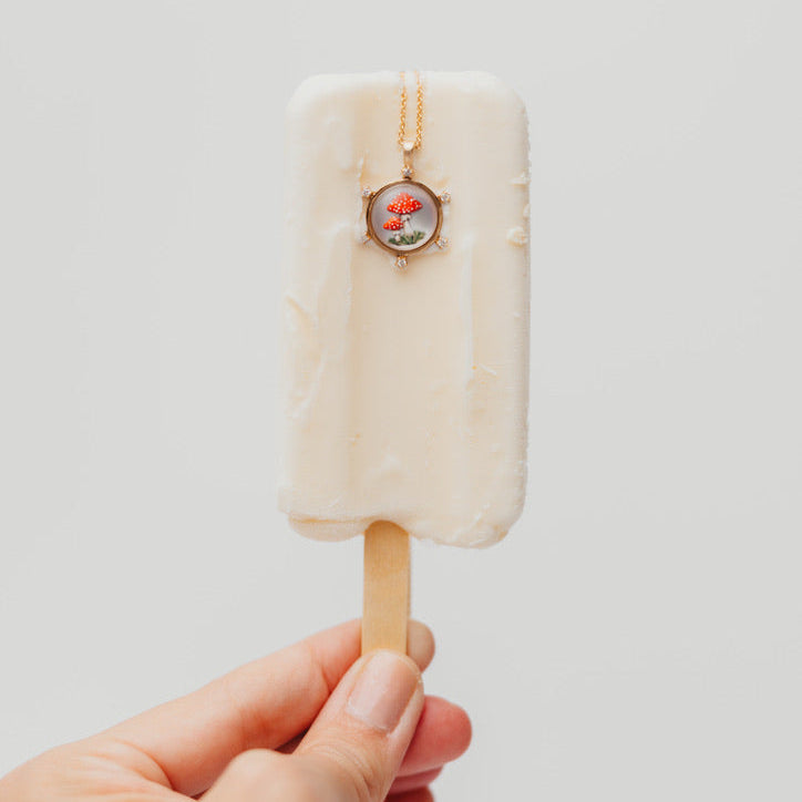 Hand holding a popsicle with a mushroom pendant on a light background