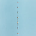 A delicate gold chain bracelet featuring nine evenly spaced, small circular enamel medallions in various colors on a solid light blue background.