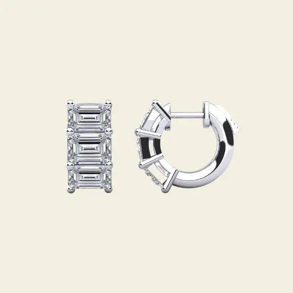 Diamond huggie earrings with baguette cut stones on a beige background. 3-Stone Emerald Huggies. Solid gold and natural diamonds. Jewelry Dallas.