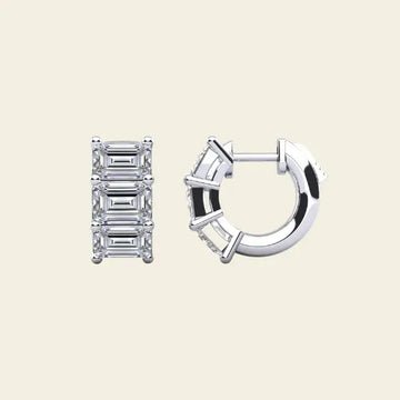 Diamond huggie earrings with baguette cut stones on a beige background. 3-Stone Emerald Huggies. Solid gold and natural diamonds. Jewelry Dallas.