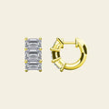 Diamond huggie earrings with baguette cut stones on a beige background. 3-Stone Emerald Huggies. Solid gold and natural diamonds. Jewelry Dallas.