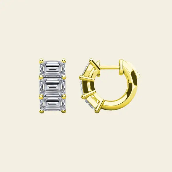 Diamond huggie earrings with baguette cut stones on a beige background. 3-Stone Emerald Huggies. Solid gold and natural diamonds. Jewelry Dallas.
