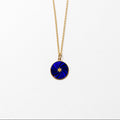 A gold chain necklace with a circular pendant featuring a deep blue and black swirled design with a small gold star in the center, shown against a plain white background.