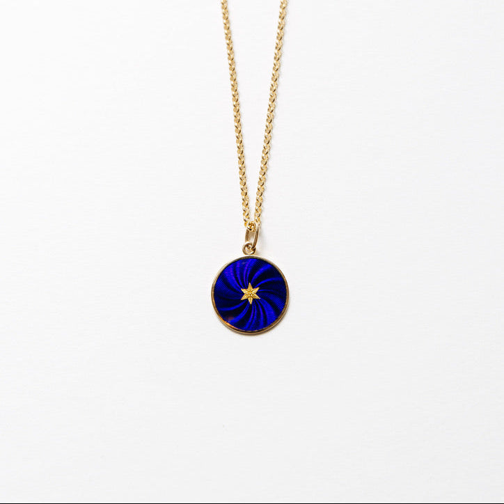 A gold chain necklace with a circular pendant featuring a deep blue and black swirled design with a small gold star in the center, shown against a plain white background.
