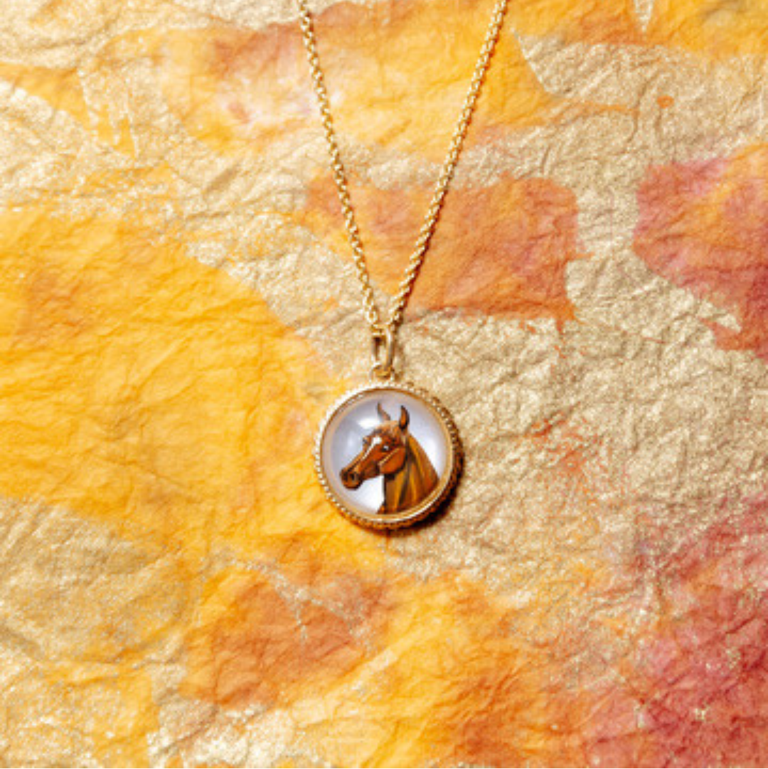Gold necklace with a pendant featuring an image of a horse on a beige background