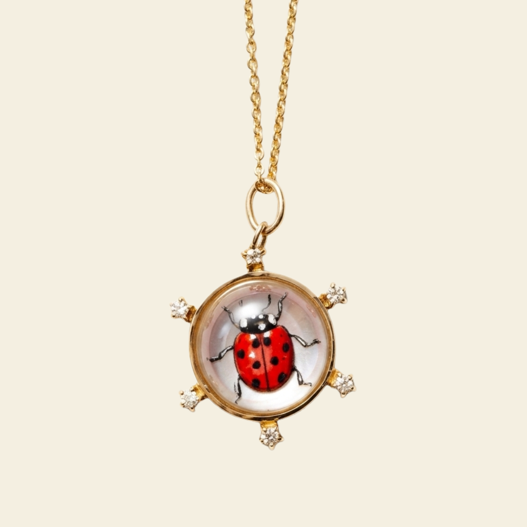 Gold necklace with a pendant featuring a ladybug design on a beige background