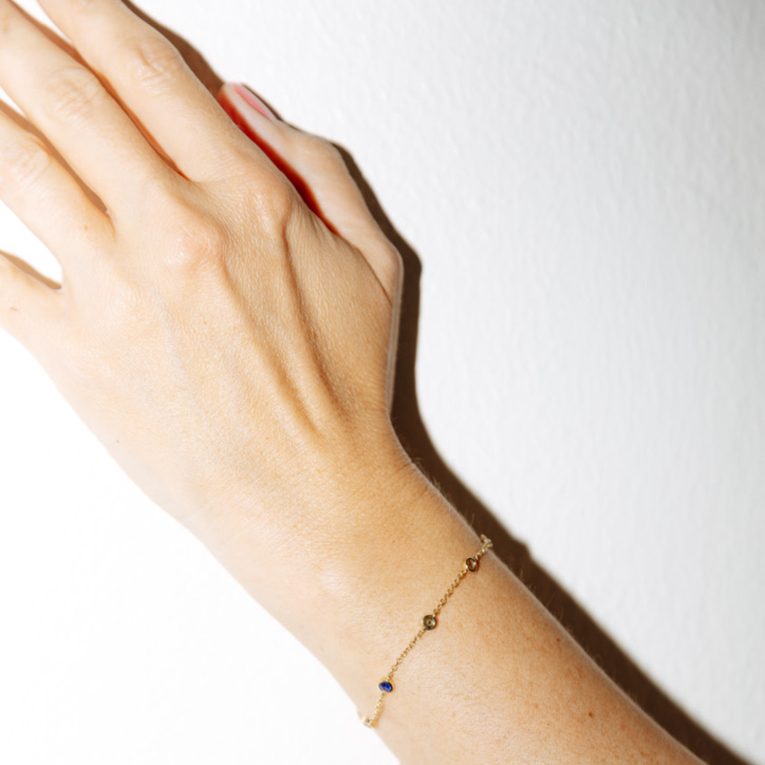 Hand wearing a delicate rainbow sapphire bracelet on a plain background