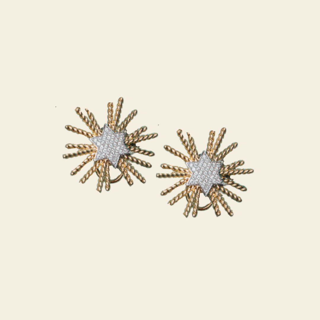 A pair of gold and white starburst stud earrings on a solid cream background.