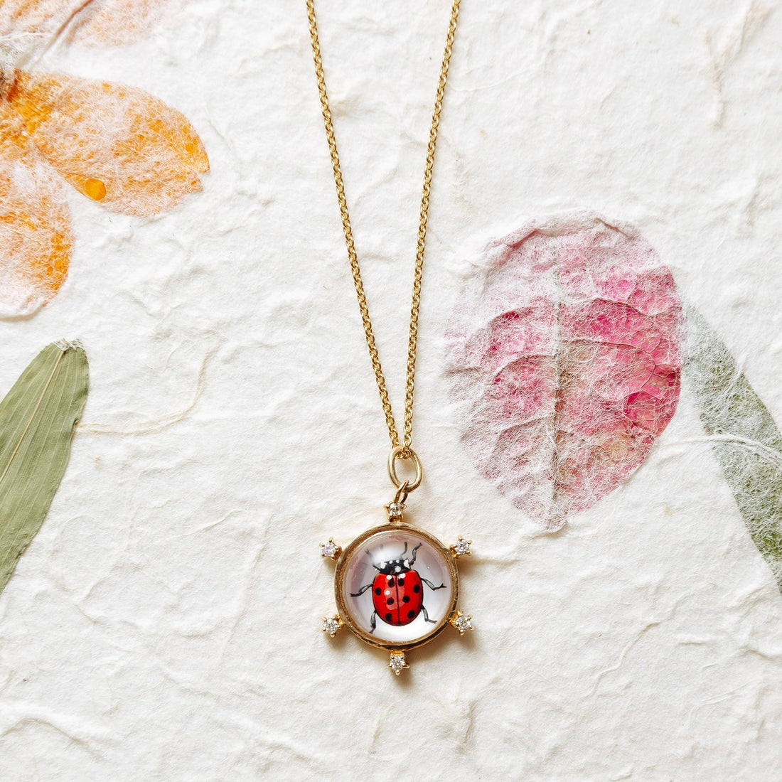 Gold necklace with a pendant featuring a ladybug design on a beige background