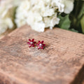 Pair of red earrings on a wooden surface with white flowers in the background