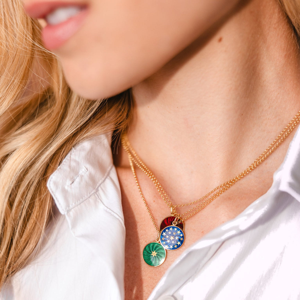A close-up lifestyle shot of a woman wearing a layered gold necklace with three colorful circular enamel pendants: green, blue, and red.