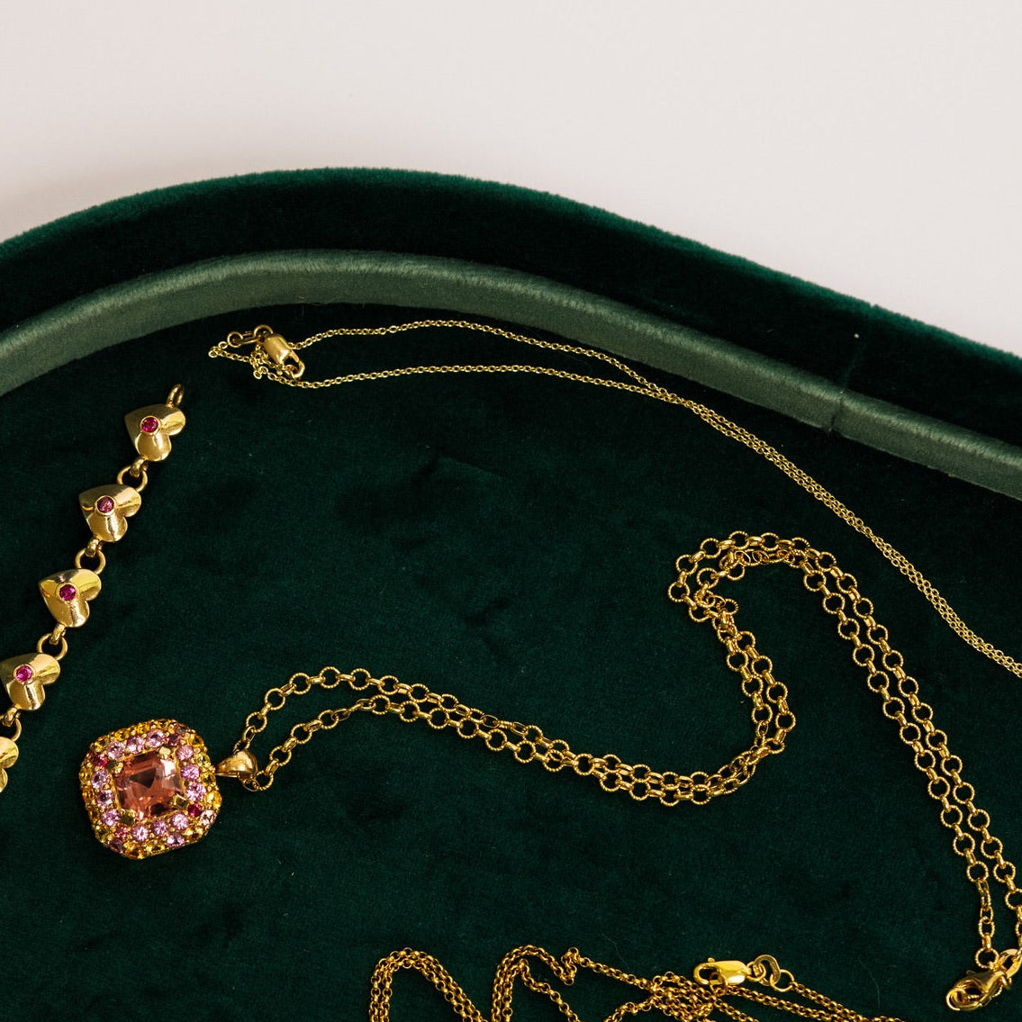 A collection of gold jewelry, including necklaces, bracelets, and a ring, arranged on a dark green velvet jewelry tray.
