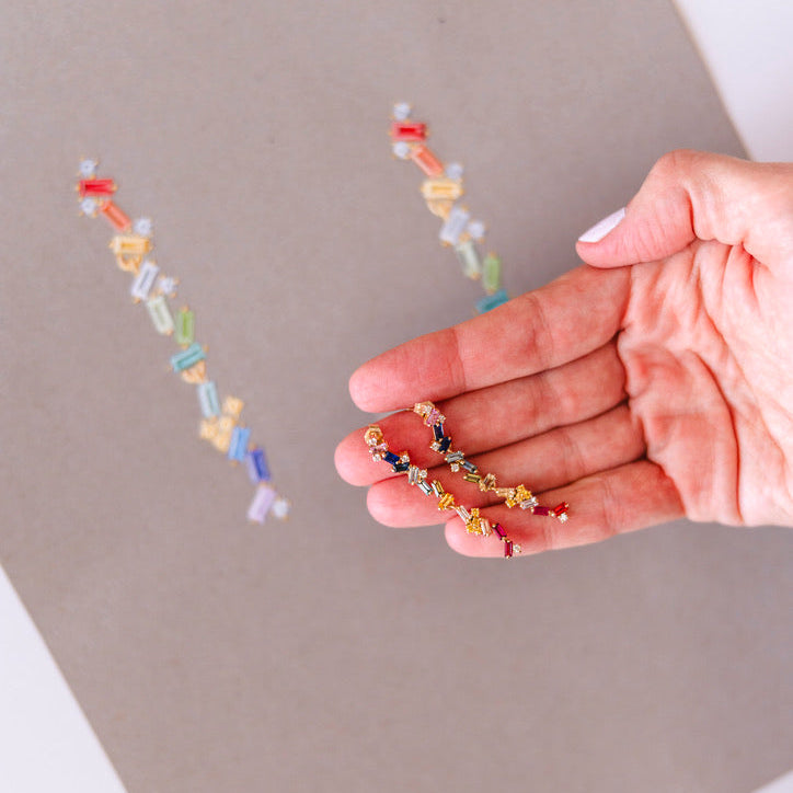 Hand holding a colorful earrings with another necklace on a gray surface