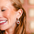 A close-up lifestyle shot of a woman with long auburn hair wearing a Pink Tourmaline Hexagon Drop Earring with Diamonds surrounded by small clear stones.