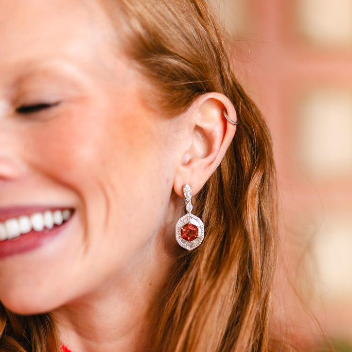 A close-up lifestyle shot of a woman with long auburn hair wearing a Pink Tourmaline Hexagon Drop Earring with Diamonds surrounded by small clear stones.