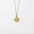 A delicate gold chain necklace featuring a small, circular, olive-green pendant with a sunburst pattern, displayed against a clean white background.