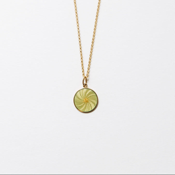 A delicate gold chain necklace featuring a small, circular, olive-green pendant with a sunburst pattern, displayed against a clean white background.