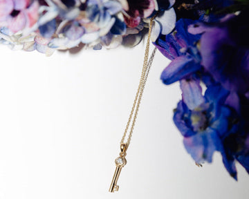 Gold necklace with a key pendant against a floral background