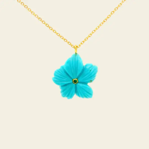 Turquoise flower-shaped pendant on a gold chain against a beige background. Arizona Turquoise Carved Flower. Hand-carved from vibrant Arizona turquoise, this floral pendant is accented with a rich emerald center for a striking pop of color. Finished with a classic 14k gold rolo chain, each piece is naturally unique and designed to be worn every day or layered with ease. Jewelry Dallas.