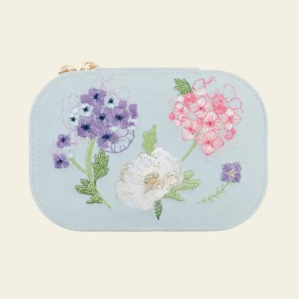 Light blue velvet travel jewelry box with floral embroidery on a beige background. Blooming with Cheer Light Blue Velvet Embroidered Travel Jewelry Box. Jewelry Dallas.