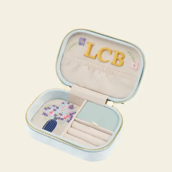 Light blue velvet travel jewelry box with floral embroidery on a beige background. Blooming with Cheer Light Blue Velvet Embroidered Travel Jewelry Box. Jewelry Dallas.
