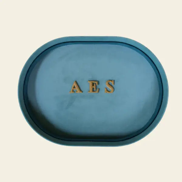 Blue oval velvet jewelry tray with 'AES' initials on a beige background. Blue Velvet Jewelry Tray. Jewelry Dallas.