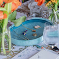 Jewelry on a blue velvet jewelry tray with flowers and glasses on a table. Blue Velvet Jewelry Tray. Jewelry Dallas.