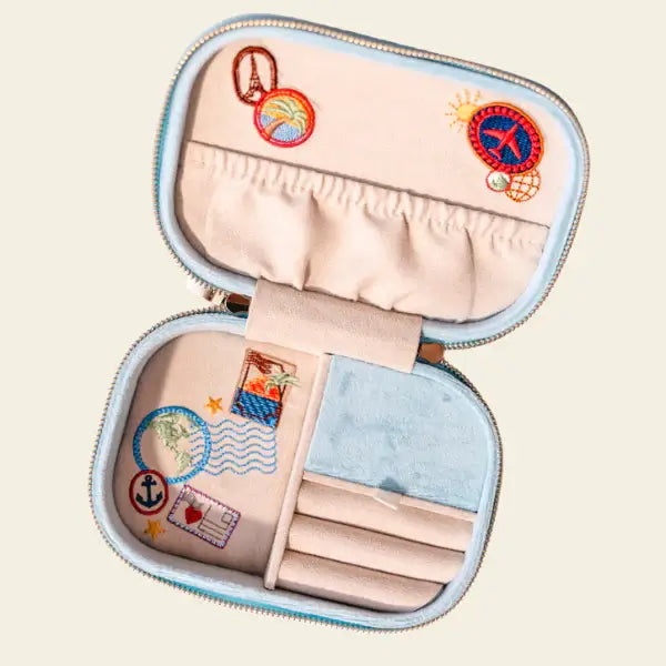 Light blue velvet travel jewelry box with embroidered designs on a beige background. Bon Voyage Light Blue Velvet Embroidered Travel Jewelry Box. Jewelry Dallas.