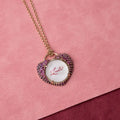 Necklace with a heart-shaped pendant on a pink background. Custom Calligraphied Essex Crystal. Materials: Solid 14kt Gold Frame with Hand-Carved Rock Crystal and Natural Pink Sapphires
Customization: Single Initial or Monogram, Reverse-Carved and Hand-Painted in Custom Calligraphy
Optional: Diamond Accents Available Upon Request
Chain: Sold Separately (Pairs Beautifully with Our Classic Cable or Paperclip Chains)
Origin: Handcrafted in the USA. Jewelry Dallas.