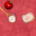 Two necklaces with 'Lucille' calligraphed on them, surrounded by natural colored gemstones. Custom Calligraphied Essex Crystal. Materials: Solid 14kt Gold Frame with Hand-Carved Rock Crystal and Natural Pink Sapphires
Customization: Single Initial or Monogram, Reverse-Carved and Hand-Painted in Custom Calligraphy
Optional: Diamond Accents Available Upon Request
Chain: Sold Separately (Pairs Beautifully with Our Classic Cable or Paperclip Chains)
Origin: Handcrafted in the USA. Jewelry Dallas.