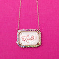 Necklace with a pendant displaying the name 'Lucille' on a pink background. Custom Calligraphied Essex Crystal. Materials: Solid 14kt Gold Frame with Hand-Carved Rock Crystal and Natural Pink Sapphires
Customization: Single Initial or Monogram, Reverse-Carved and Hand-Painted in Custom Calligraphy
Optional: Diamond Accents Available Upon Request
Chain: Sold Separately (Pairs Beautifully with Our Classic Cable or Paperclip Chains)
Origin: Handcrafted in the USA. Jewelry Dallas.
