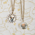 Two necklaces with circular pendants featuring dog portraits on a decorative background. Custom Pet Portrait. Hand-carved in Germany and painted in reverse intaglio on rock crystal, each charm is backed with luminous mother-of-pearl and set in your choice of 18K yellow, rose, or white gold. Jewelry Dallas.