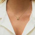 Gold necklace with a letter 'A' pendant worn by a person in a white outfit. Diamond Letter Pendant. Length and Layering: 16