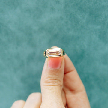 Hand holding a ring with a moonstone against a teal background