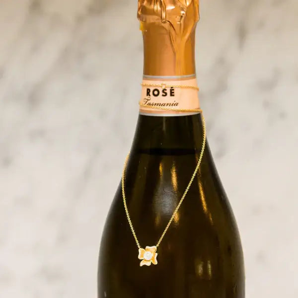 Bottle of Rosé wine with a gold necklace draped over it against a neutral background. Flower Power. Length: 16"+2" Link Chain Materials: Solid 14kt Gold with Natural Diamonds. Jewelry Dallas.