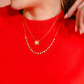 Person wearing a red sweater with a gold necklace featuring a flower-shaped pendant. 