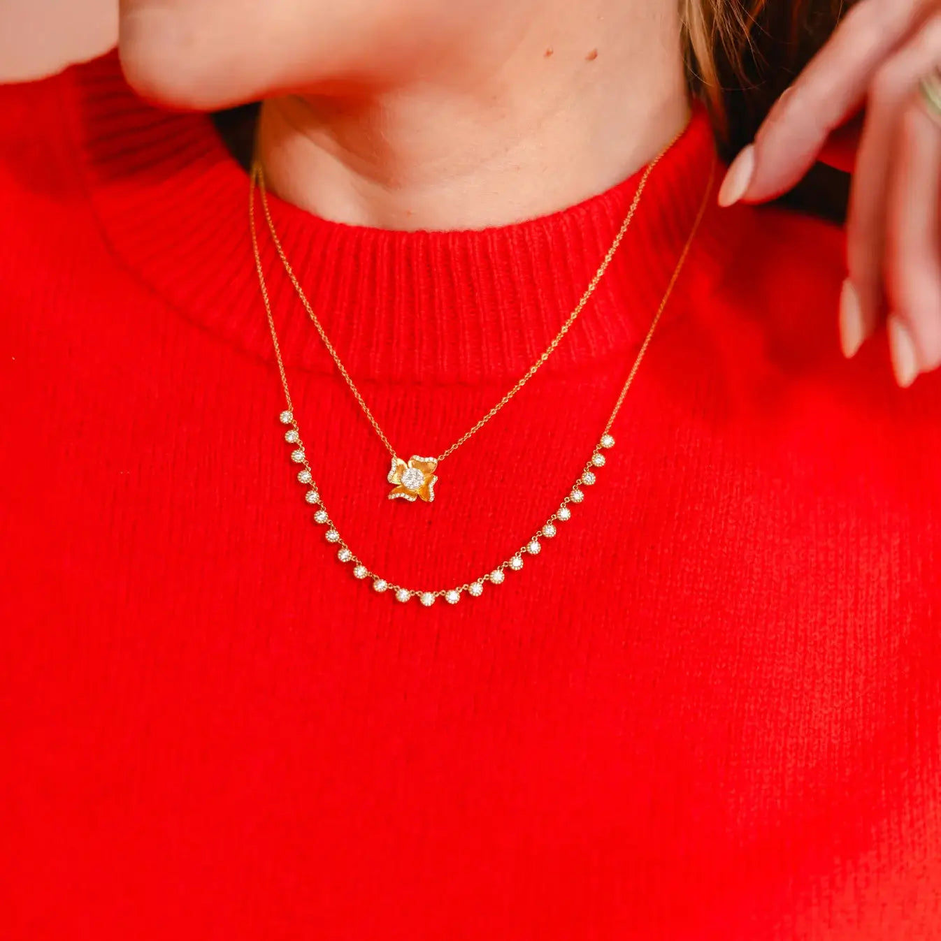 Person wearing a red sweater with a gold necklace featuring a flower-shaped pendant. 