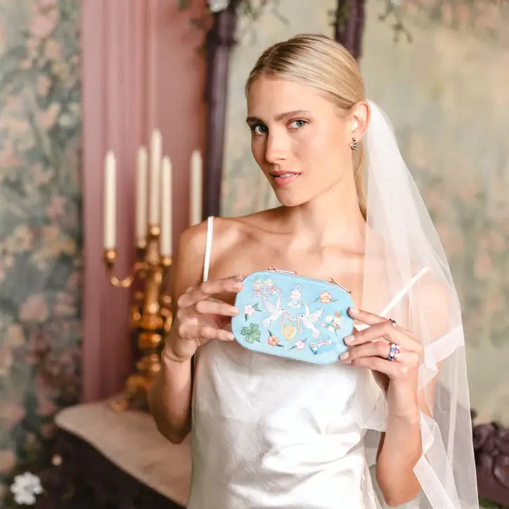 Bride holding a blue velvet travel jewelry box with floral embroidery in a vintage room. Forever After Blue Velvet Embroidered Travel Jewelry Box. Jewelry Dallas. 