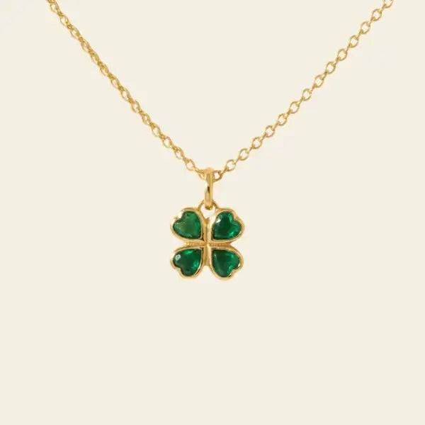 Gold necklace with a green four-leaf clover pendant on a beige background. Four Heart Clover. Crafted in 14k gold and set with 0.74 carats of sparkling natural emeralds. Jewelry Dallas.