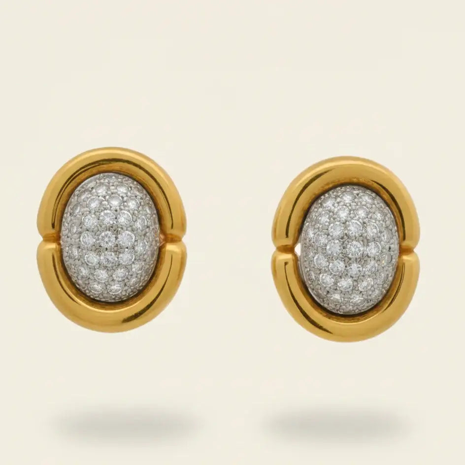 Gold earrings with diamond-pave centers on a beige background. Gold & Diamond Pavé Oval Earrings. These oval earrings are crafted in rich 14k yellow gold and set with 1 carat of natural pavé diamonds for radiant sparkle. Jewelry Dallas.