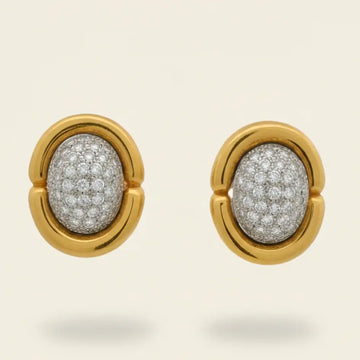 Gold earrings with diamond-pave centers on a beige background. Gold & Diamond Pavé Oval Earrings. These oval earrings are crafted in rich 14k yellow gold and set with 1 carat of natural pavé diamonds for radiant sparkle. Jewelry Dallas.