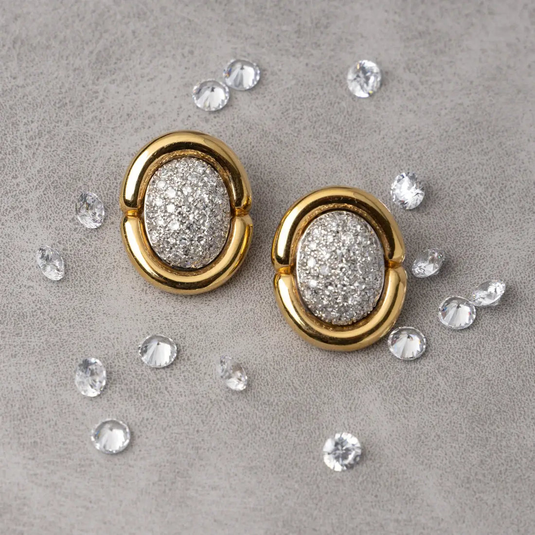 Gold earrings with diamond-pave centers on a beige background. Gold & Diamond Pavé Oval Earrings. These oval earrings are crafted in rich 14k yellow gold and set with 1 carat of natural pavé diamonds for radiant sparkle. Jewelry Dallas.