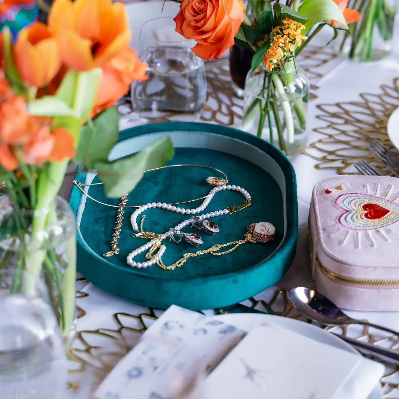 Jewelry on a green velvet jewelry tray with flowers and a heart-embroidered pink travel jewelry box on a table. Green Velvet Jewelry Tray. Jewelry Dallas.