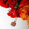 Gold necklace with pink gemstones in front of red and orange flowers on a white background