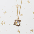 A gold chain necklace with a celestial pendant featuring a crescent moon, displayed on a white background with gold star illustrations.
