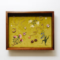 A jewelry tray showcasing various handmade jewelry pieces, including necklaces, rings, and earrings, arranged on a textured olive green velvet background with embroidered floral motifs.