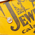 A gold pendant necklace with a round bezel containing a preserved butterfly, displayed on a textured yellow background with bold black text.