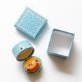 A light blue textured ring box set on a white background, featuring one closed lid, one open lid displaying a gold interior, and one ring resting on a gold circular insert.