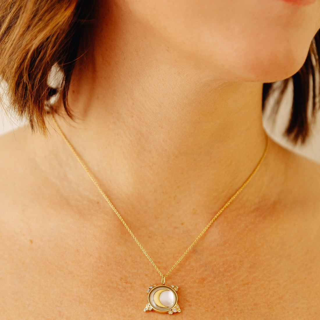 Gold necklace with a pendant featuring a moon design on a beige background