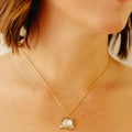 A close-up lifestyle shot of a model wearing a delicate gold chain necklace with a small pendant featuring a white pearl and gold moon.
